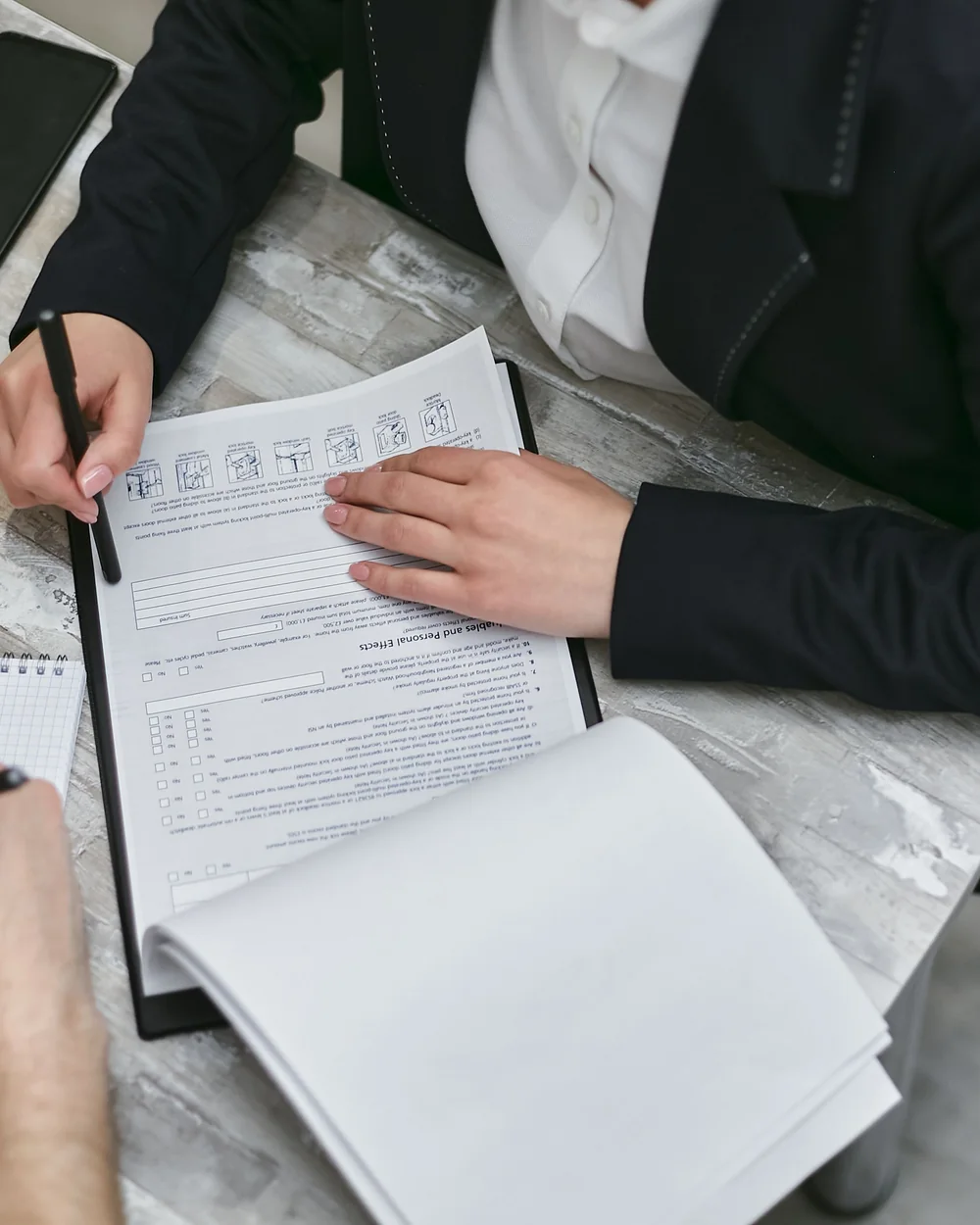Two adults' hands reviewing a printed form beside an open notebook on a gray table
