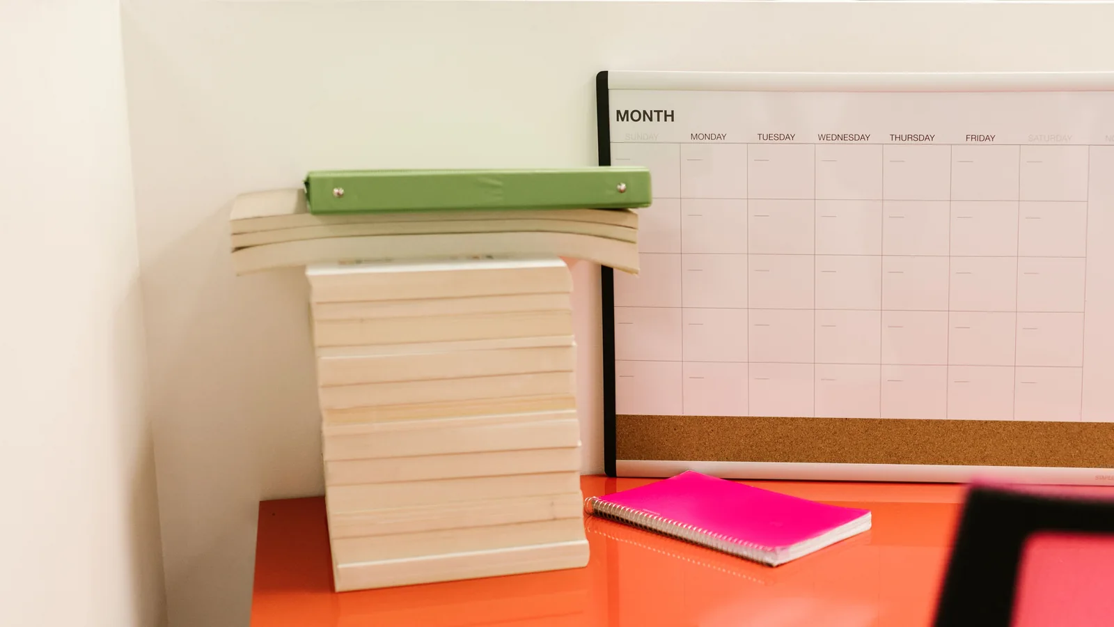 Blank monthly wall calendar above a desk with books and a green binder