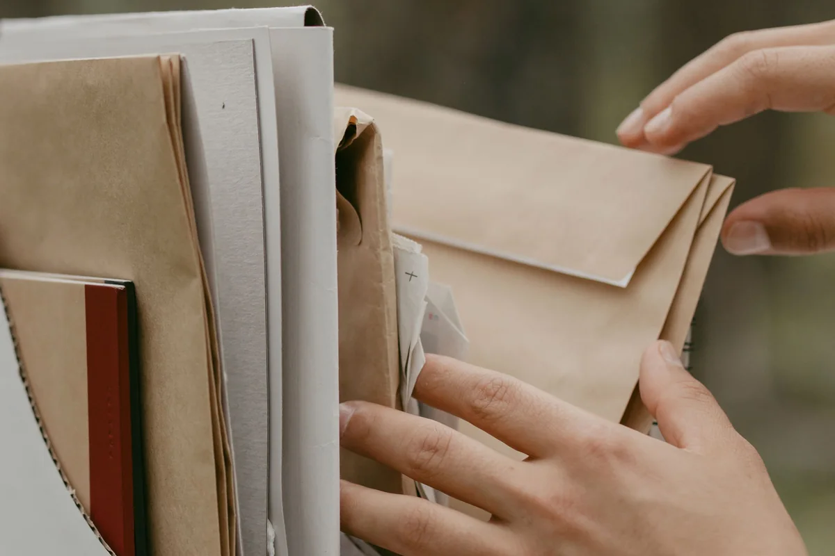 Hands sorting a kraft envelope among folders and papers in two white file boxes