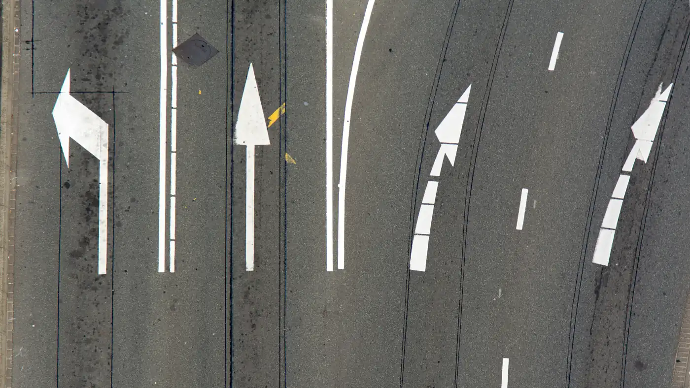 Overhead view of road lane markings with a left-turn arrow beside straight and curving lane arrows