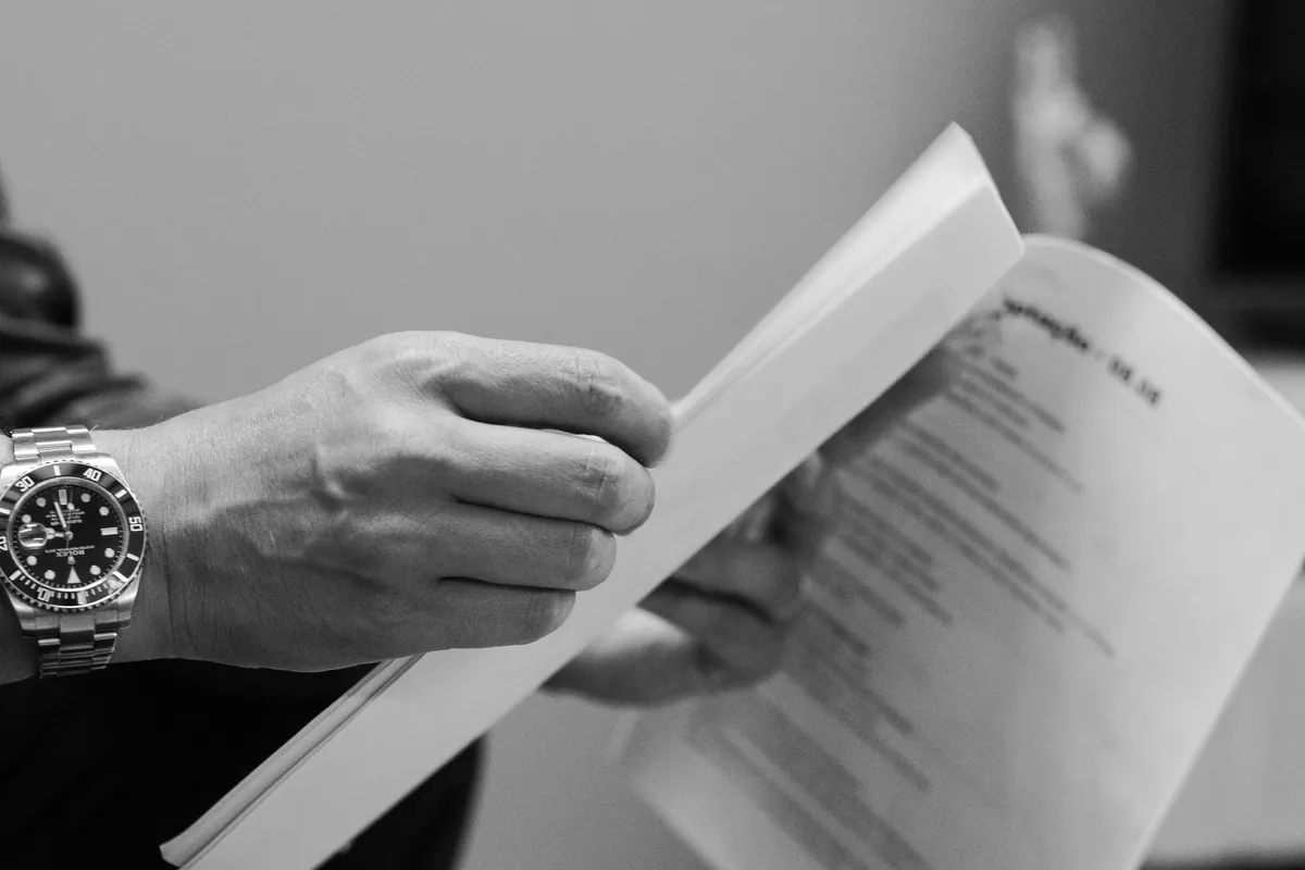 Hands reviewing printed documents beside a wristwatch