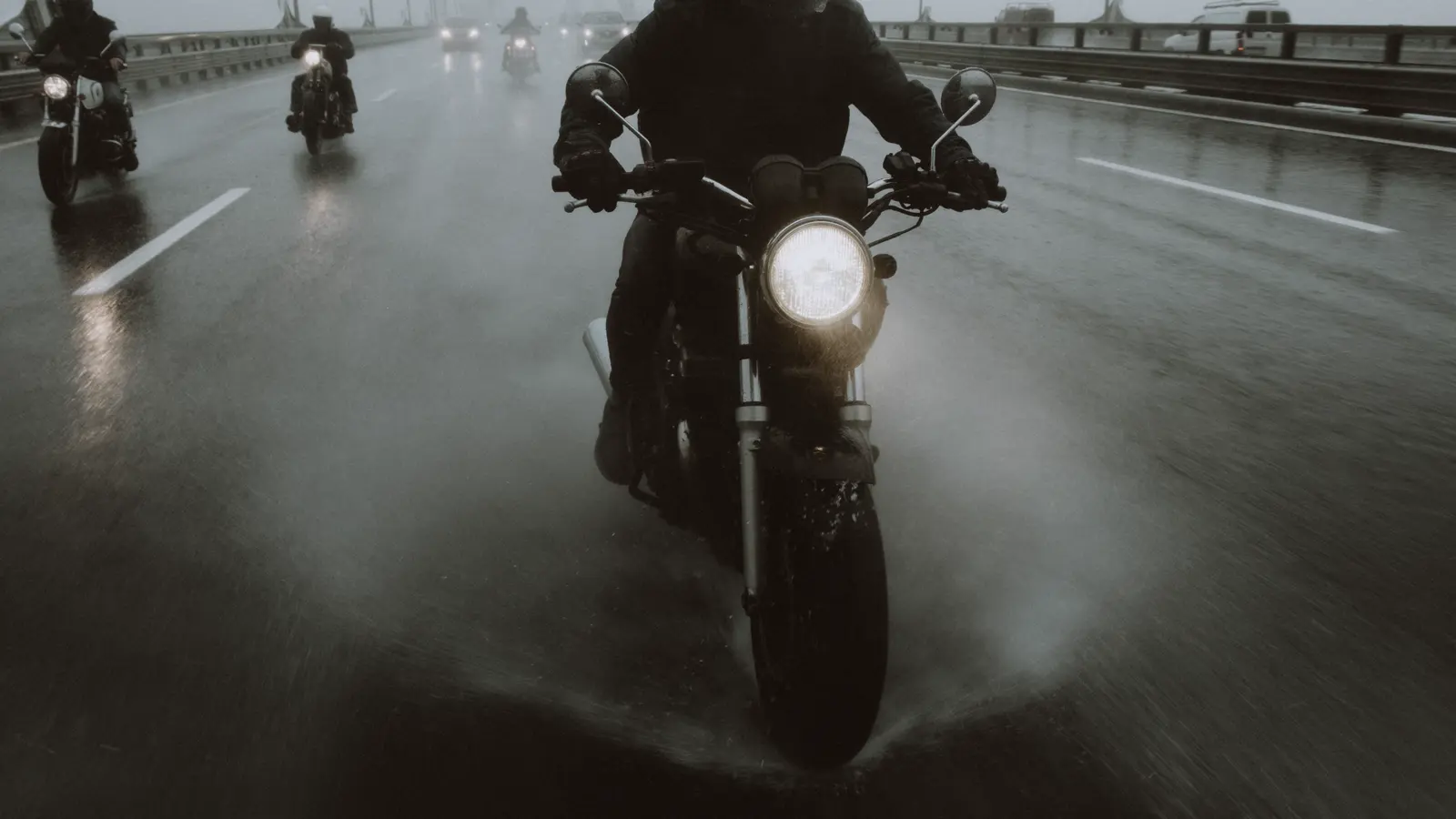 Helmeted motorcycle riders traveling on a wet multilane road