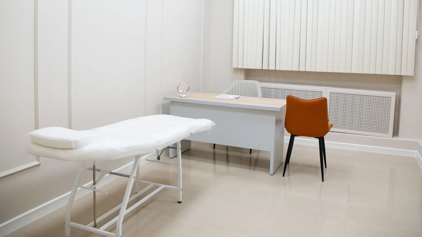 Empty medical examination room with a padded exam table, a desk and chairs