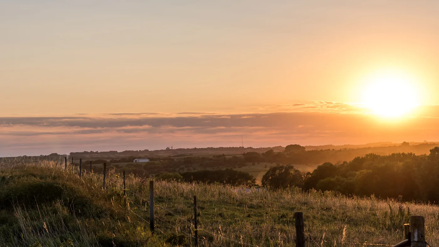 Sunrise over rural Nebraska grassland with a wire fence and a line of trees