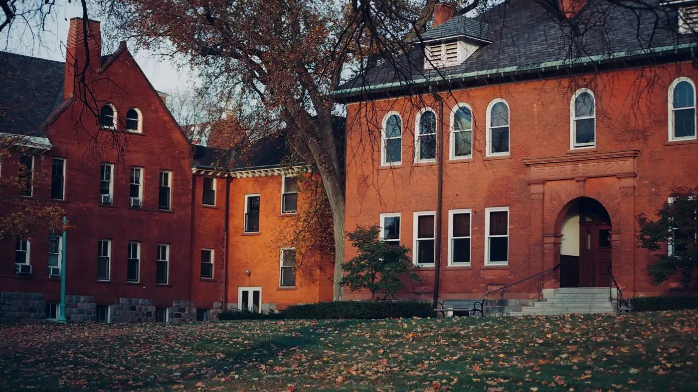 Historic red brick university building with an arched entrance and autumn leaves on the lawn