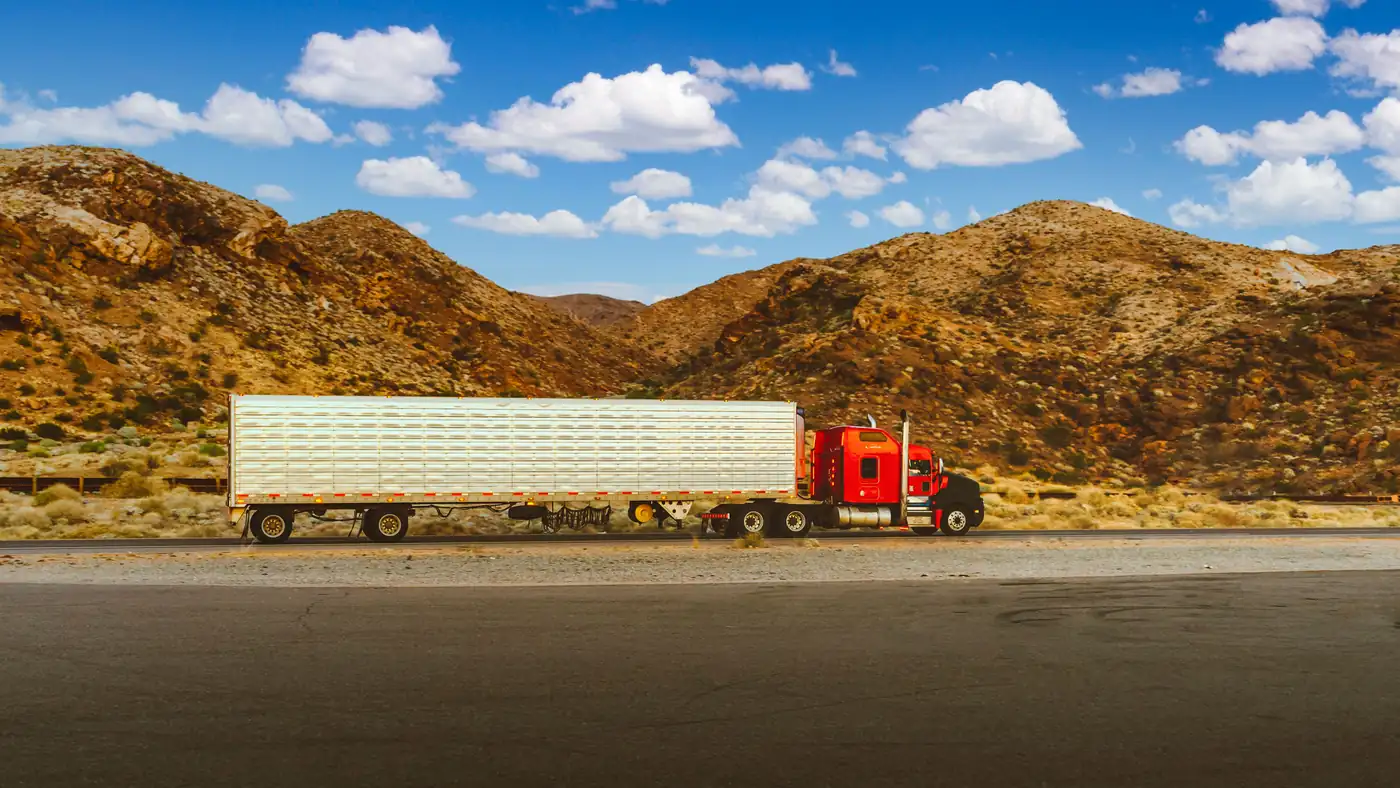 Red semi truck pulling a long silver trailer on a desert highway